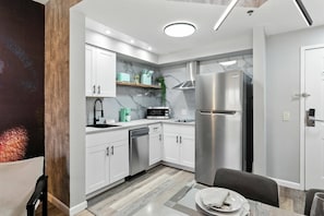 Una cocina moderna con armarios blancos, un refrigerador de acero inoxidable, un microondas y un lavavajillas.