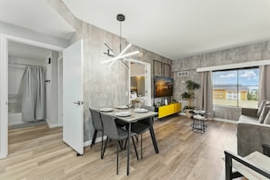 Una sala moderna con comedor, una pared de acento amarilla, un ventanal con vistas y un sofá gris.