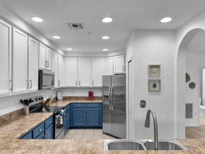 A modern kitchen with white cabinets, a stainless steel refrigerator, and granite countertops. - Themed 2BR condo | Star Wars mural, 15 min Disney (Kissimmee)