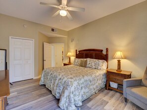 A bedroom with a bed, two bedside tables with lamps, a chair, a ceiling fan, and a door. - 2BR condo near Disney | Resort pool & sauna (Kissimmee)