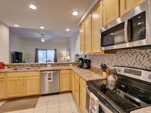 A modern kitchen with wooden cabinets, stainless steel appliances, and a herringbone backsplash. - 2BR condo near Disney | Resort pool & sauna (Kissimmee)