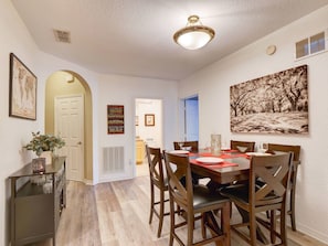 A dining area with a wooden table, chairs, and a ceiling light fixture. - 2BR condo near Disney | Resort pool & sauna (Kissimmee)