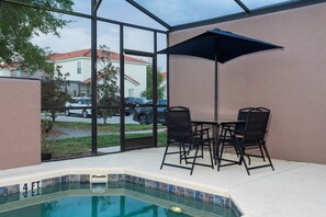Un área de piscina interior con un jacuzzi, una mesa con sillas y un paraguas grande.