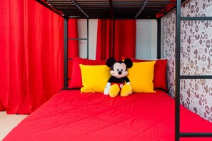 Una cama con ropa de cama roja y un peluche de Mickey Mouse.