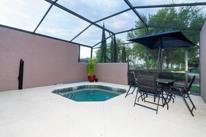 Una piscina interior con cerramiento de vidrio, rodeada por un patio con sillas y una mesa.