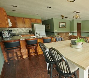 A kitchen with wooden cabinets, a refrigerator, a dining table with chairs, and a bar area.