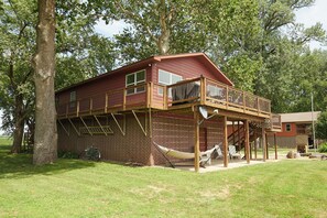 A two-story wooden cabin with a balcony, surrounded by trees.