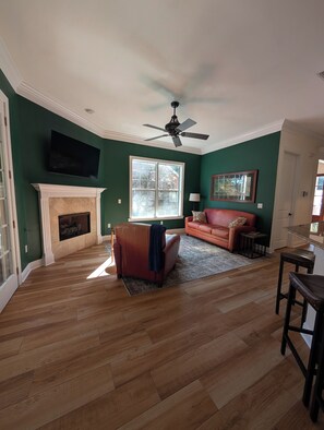 A living room with a fireplace, a sofa, a television, and a ceiling fan. - Midtown 4BR • 3 Baths • Screened Porch • Near FSU (Tallahassee)