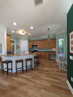 A spacious kitchen with a central island, wooden cabinets, and a dining area with white chairs. - Midtown 4BR • 3 Baths • Screened Porch • Near FSU (Tallahassee)