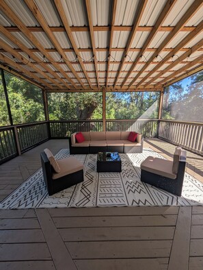 A covered outdoor seating area with a cushioned sofa and two armchairs, a patterned rug, and a wooden deck. - Walkable Midtown Retreat-Spacious 4BR/3BA & Screened Porch- Near FSU & Downtown (Tallahassee)