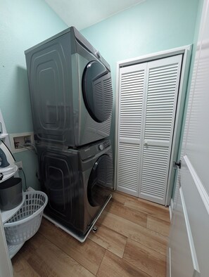 A laundry area with stacked washers and dryers, a white door, and a wooden floor. - Walkable Midtown Retreat-Spacious 4BR/3BA & Screened Porch- Near FSU & Downtown (Tallahassee)