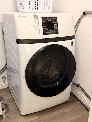 A front-loading white GE Profile washer with a control panel, a basket on top, and a hose connected to the side.