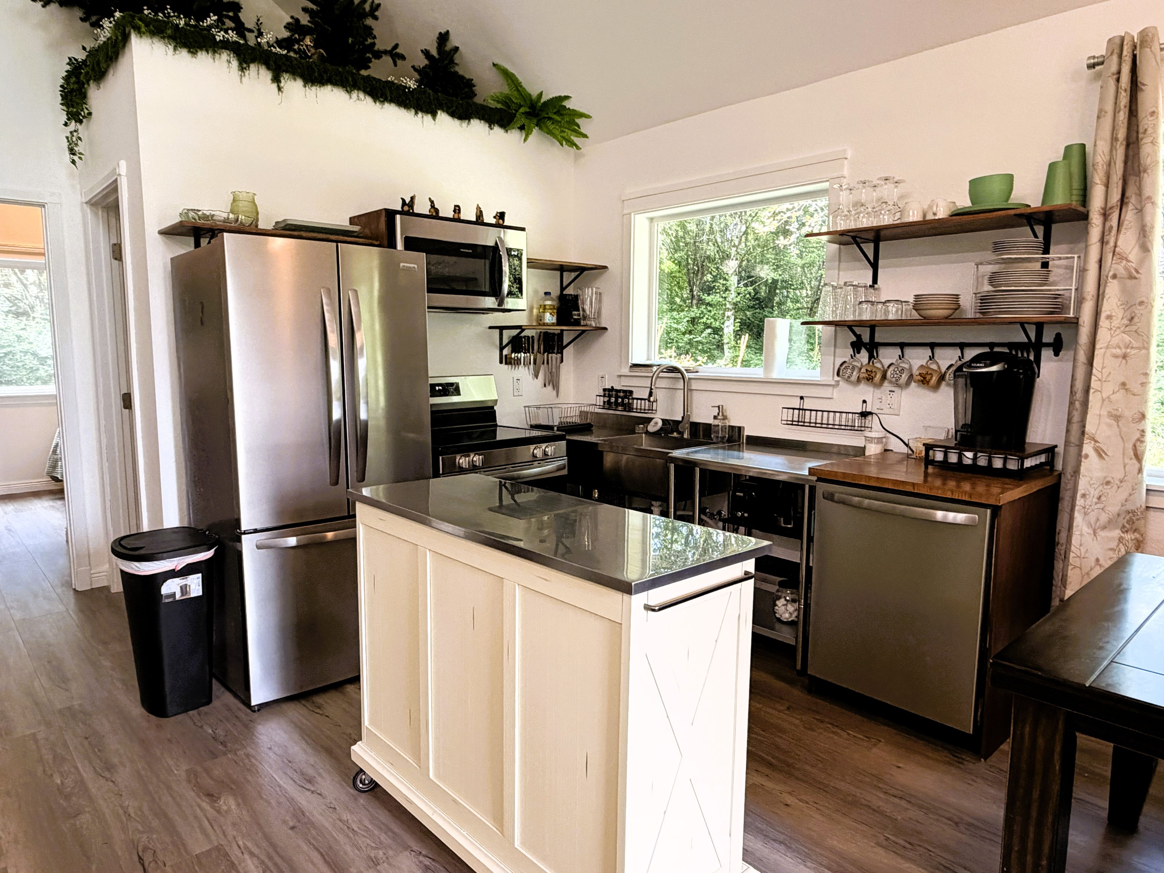 A modern kitchen with stainless steel appliances, a central island, and a window providing a view of greenery outside.