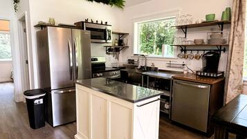 A modern kitchen with stainless steel appliances, a central island, and a window providing a view of greenery outside.