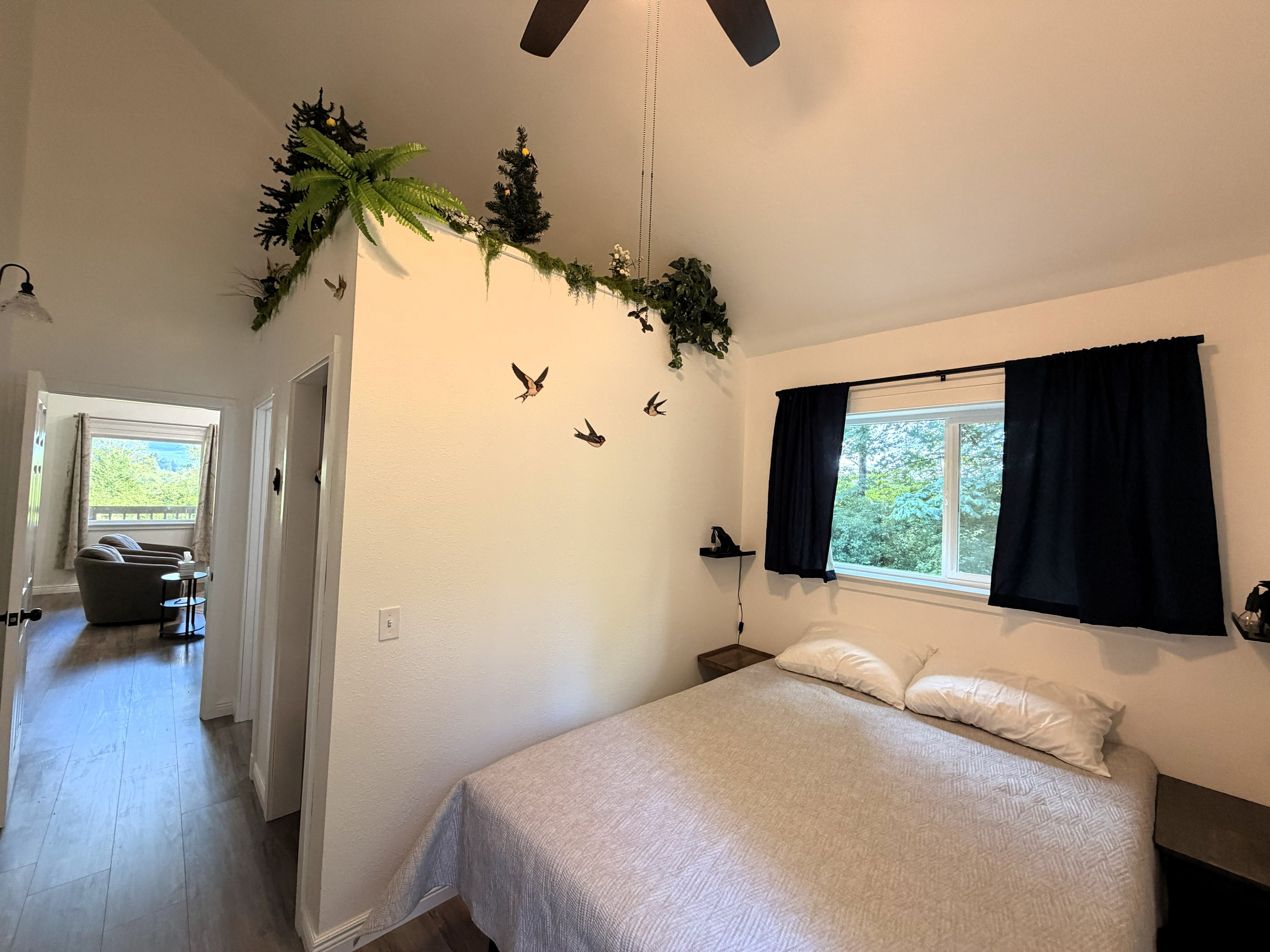 A bedroom with a bed, a window with curtains, a ceiling fan, and wall decorations including birds and greenery.