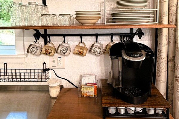 A kitchen with a coffee maker, mugs, and a milk jug.
