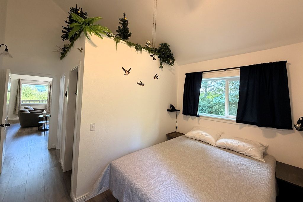 Ein Schlafzimmer mit Bett, einem Fenster mit Vorhängen, einem Wandregal und einer Tür zu einem anderen Raum.