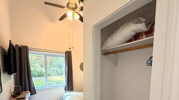 A bedroom with a bed, a ceiling fan, a window with curtains, a wooden dresser, and a closet with a shelf.