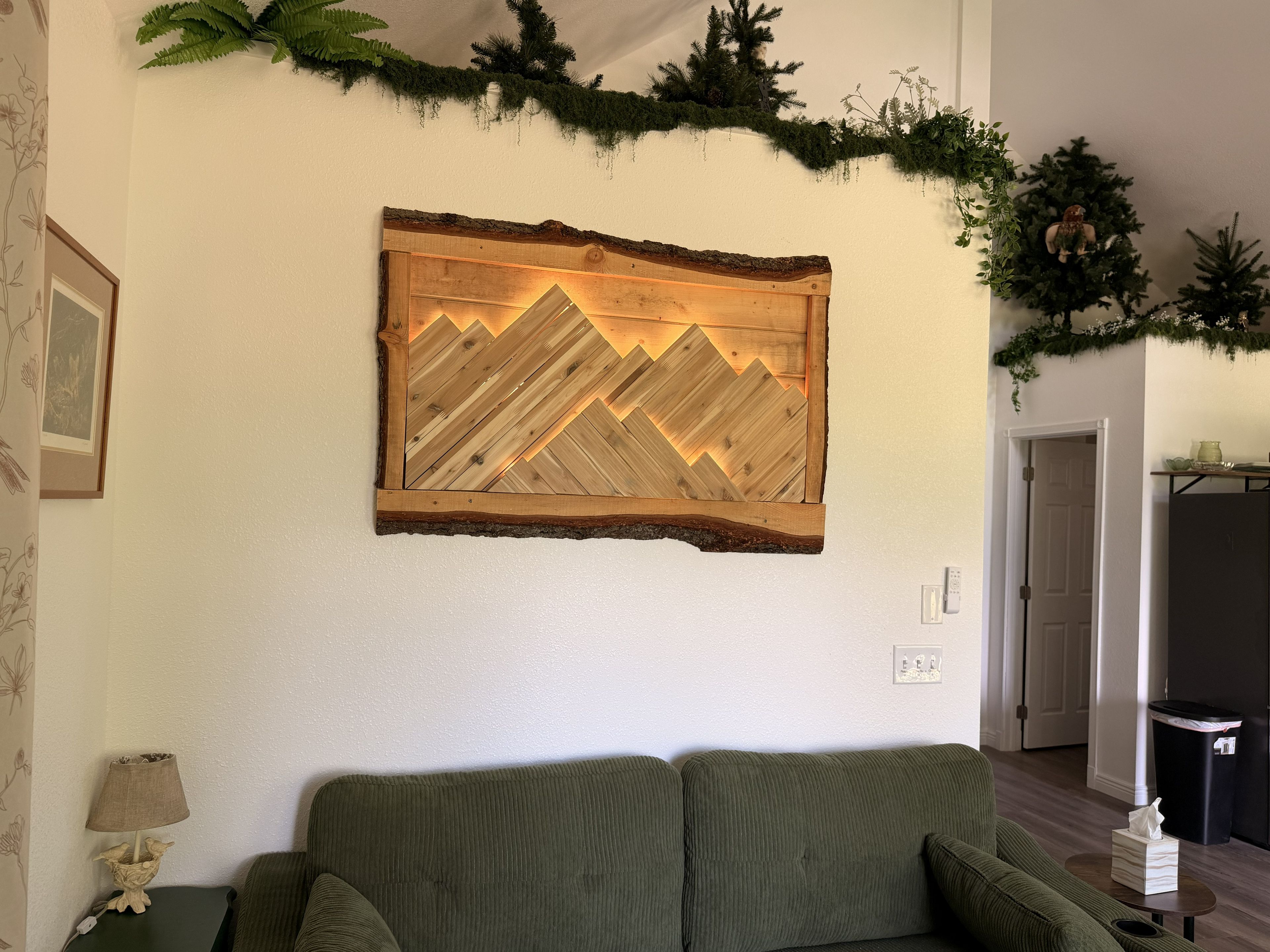 A living room with a green sofa, a wall-mounted wooden artwork, and a door leading to another room.