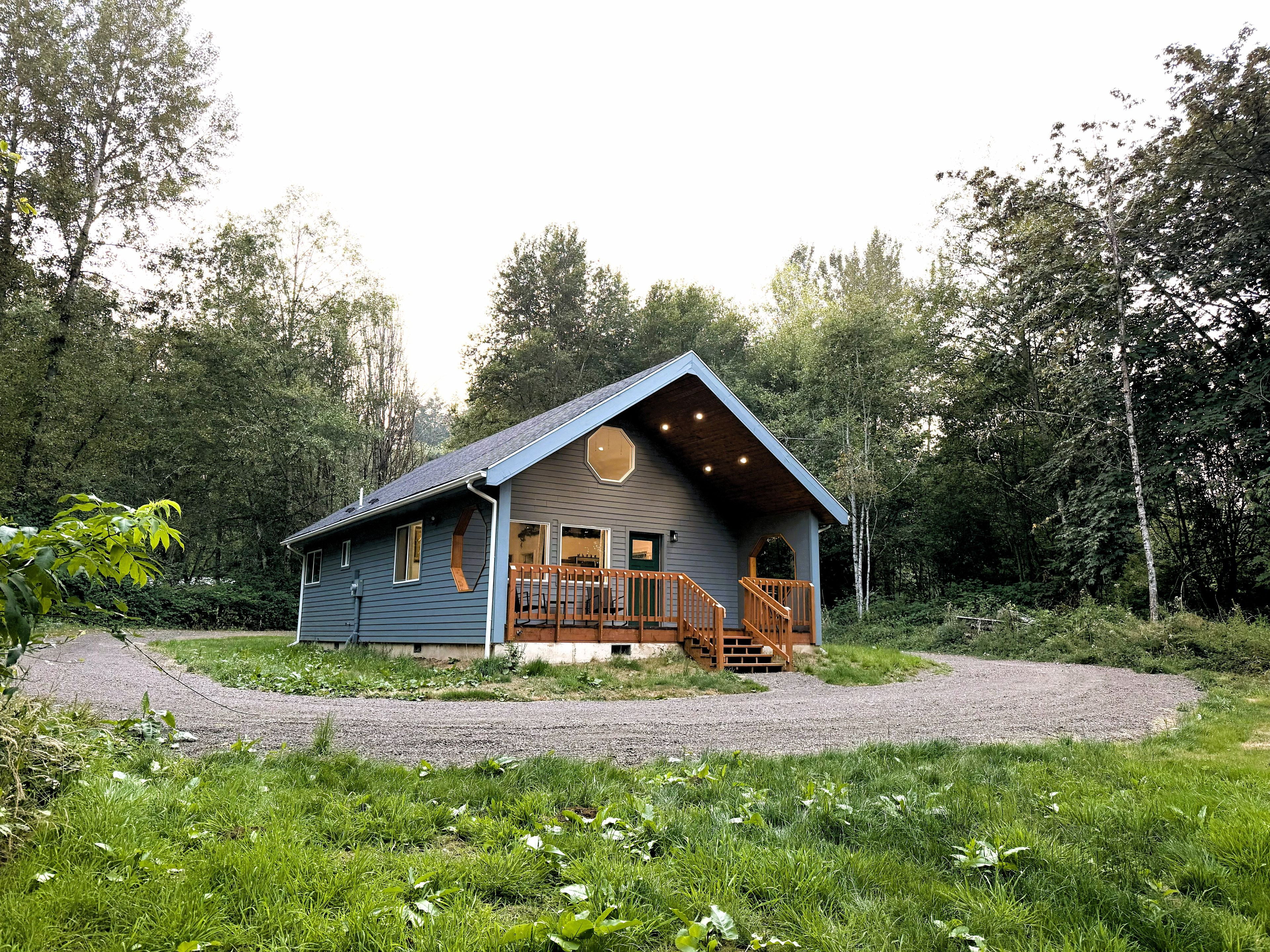 Une cabane dotée d’un porche et d’un escalier menant à une terrasse, le tout entouré d’arbres.