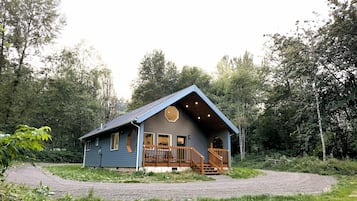 Une cabane dotée d’un porche et d’un escalier menant à une terrasse, le tout entouré d’arbres.