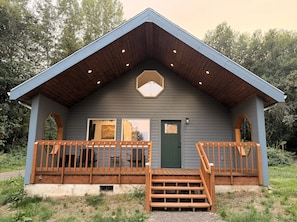 Una cabaña con terraza de madera, puerta verde y tragaluz hexagonal.