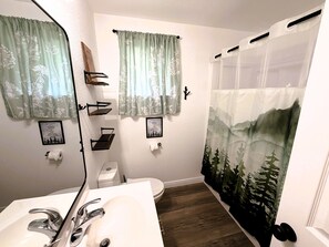 Un baño con un lavamanos blanco, dos estantes, un inodoro y una cortina de ducha con diseño de montaña.