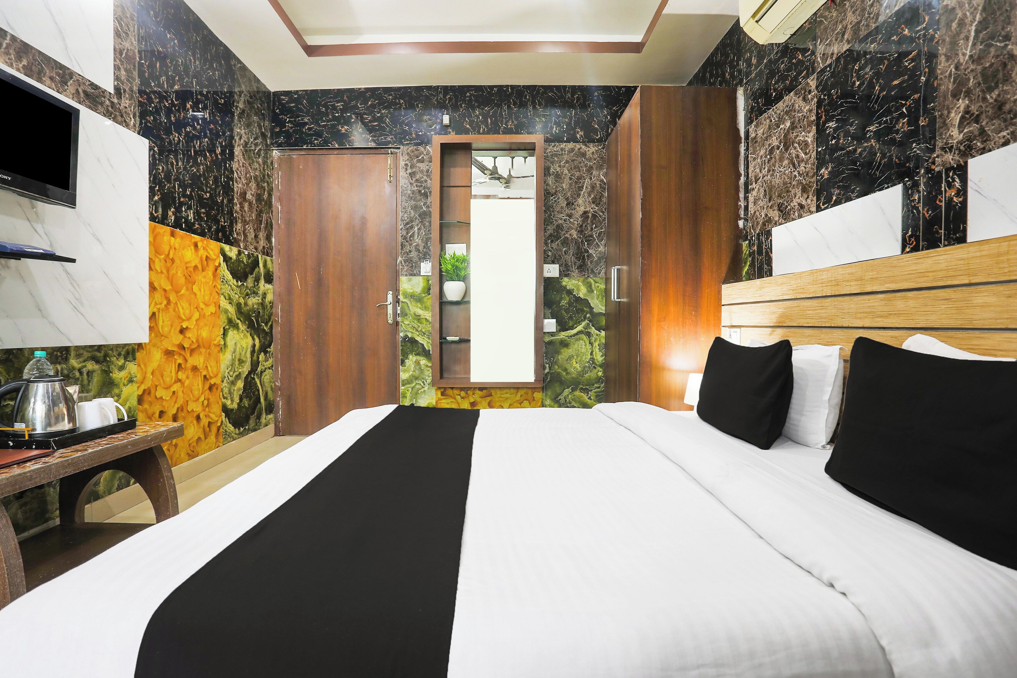 Habitación de hotel con cama, televisor, una mesa con tetera y tazas, y un mural de temática natural en la pared.