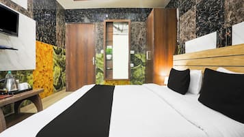 Habitación de hotel con cama, televisor, una mesa con tetera y tazas, y un mural de temática natural en la pared.