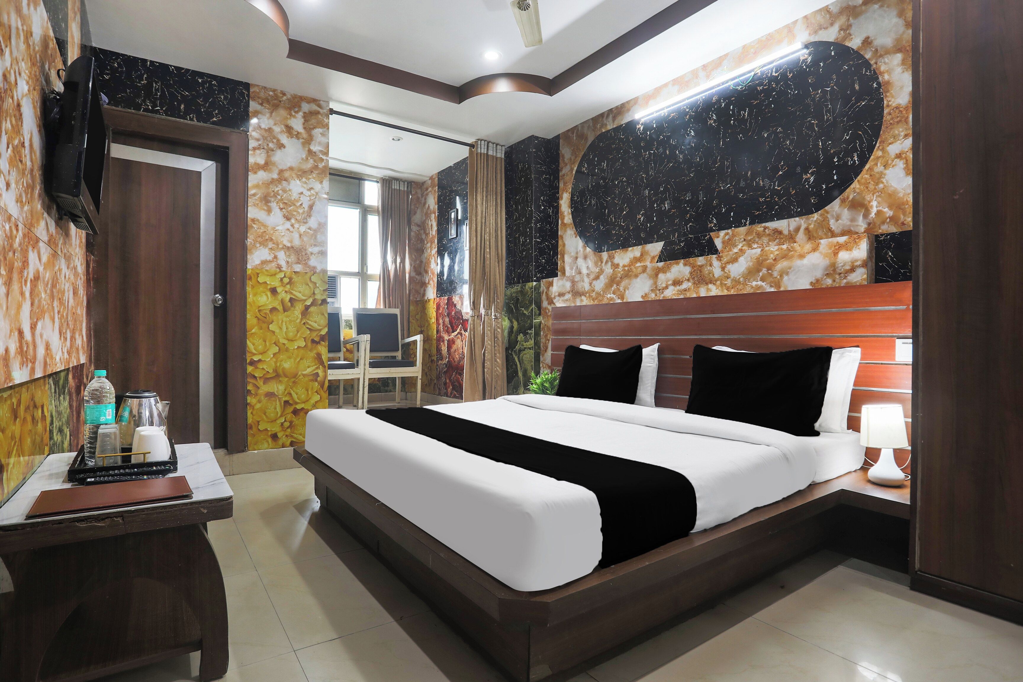 A hotel room with a large bed, a desk with a laptop, a TV mounted on the wall, and a bathroom visible through an open door.