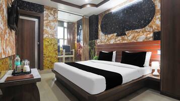 A hotel room with a large bed, a desk with a laptop, a TV mounted on the wall, and a bathroom visible through an open door.