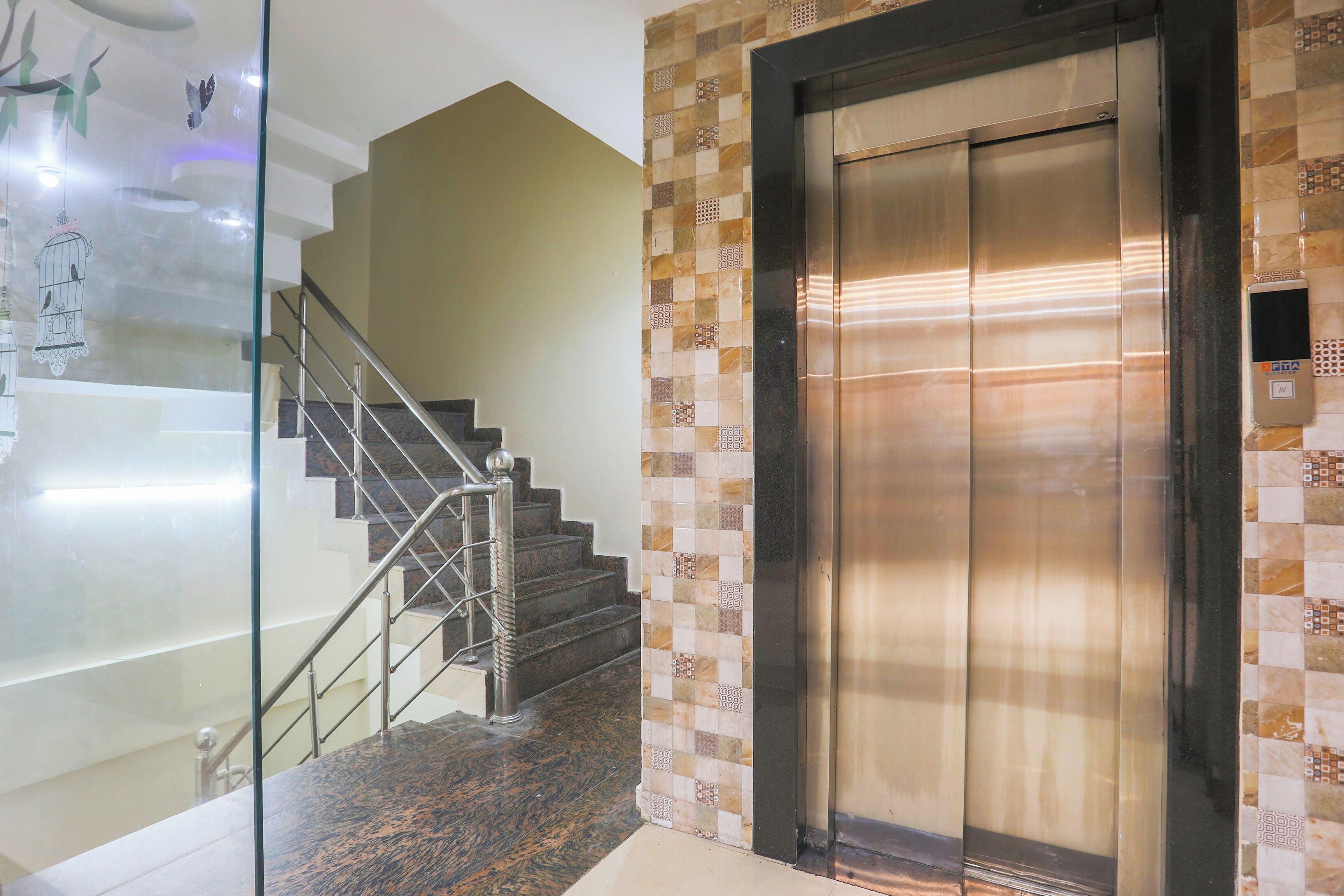 A modern elevator with a metallic finish, adjacent to a staircase with a glass railing and patterned tiles.