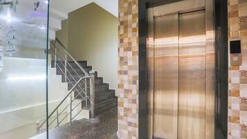 A modern elevator with a metallic finish, adjacent to a staircase with a glass railing and patterned tiles.
