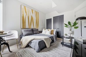 A modern bedroom with a bed, bedside tables, a chair, and a large abstract painting on the wall. - Stylish 2BR Retreat | Private Patio & Free Park (Toronto)