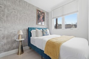 Une chambre à coucher avec un lit, une table de chevet, une lampe, une fenêtre et un tableau au mur.