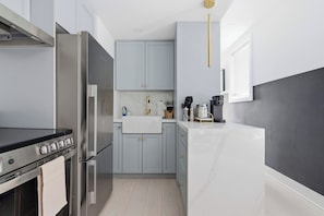A modern kitchen with stainless steel appliances, light grey cabinets, and a marble countertop.