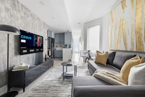 A modern living room with a flat-screen TV, grey sofa, and a coffee table. - Stylish 2BR Retreat | Private Patio & Free Park (Toronto)