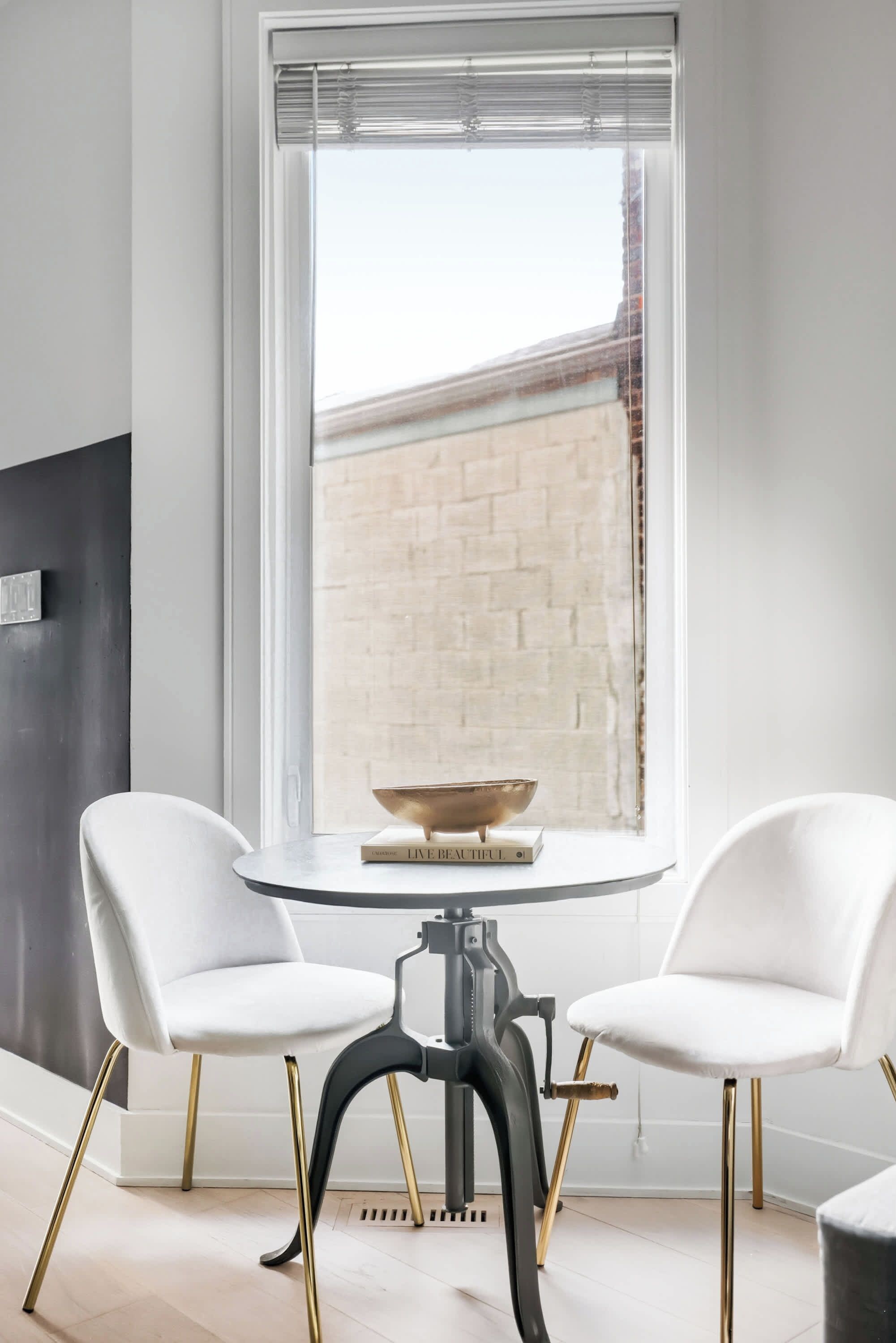A modern dining area with two white chairs, a round table, and a book titled 'LIVE BEAUTIFUL' on the table.
