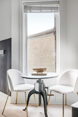 A modern dining area with two white chairs, a round table, and a book titled 'LIVE BEAUTIFUL' on the table. - Stylish 2BR Retreat | Private Patio & Free Park (Toronto)