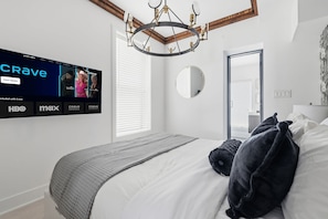 A modern bedroom with a large flat-screen TV mounted on the wall displaying a streaming service interface.