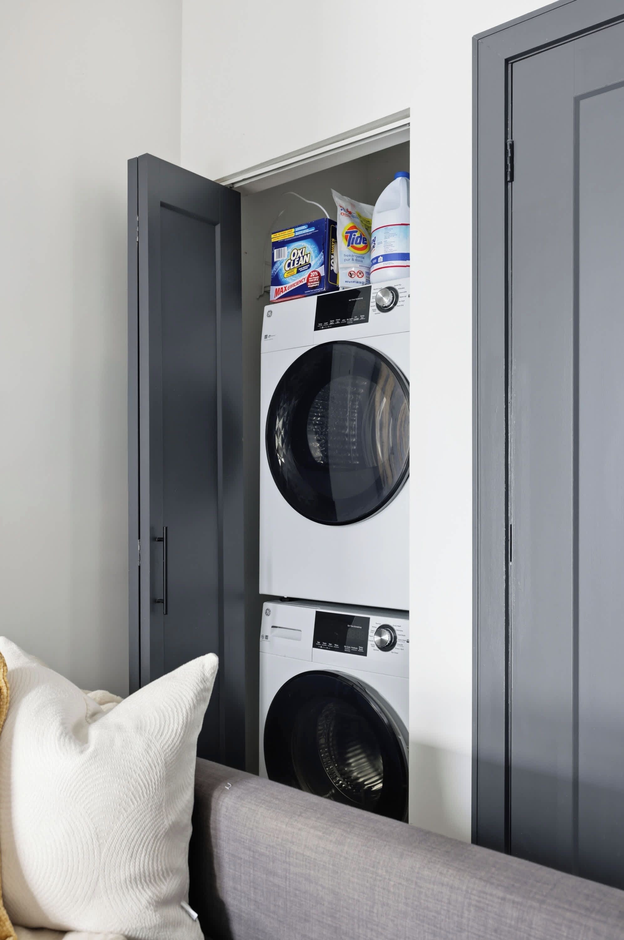 A laundry room with two stacked washing machines and detergent boxes.