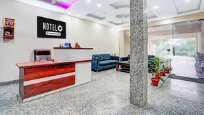 A hotel reception area with a reception desk, a blue sofa, and a ceiling fan. - Super Hotel O by OYO Fountain Chowk (Chandigarh)