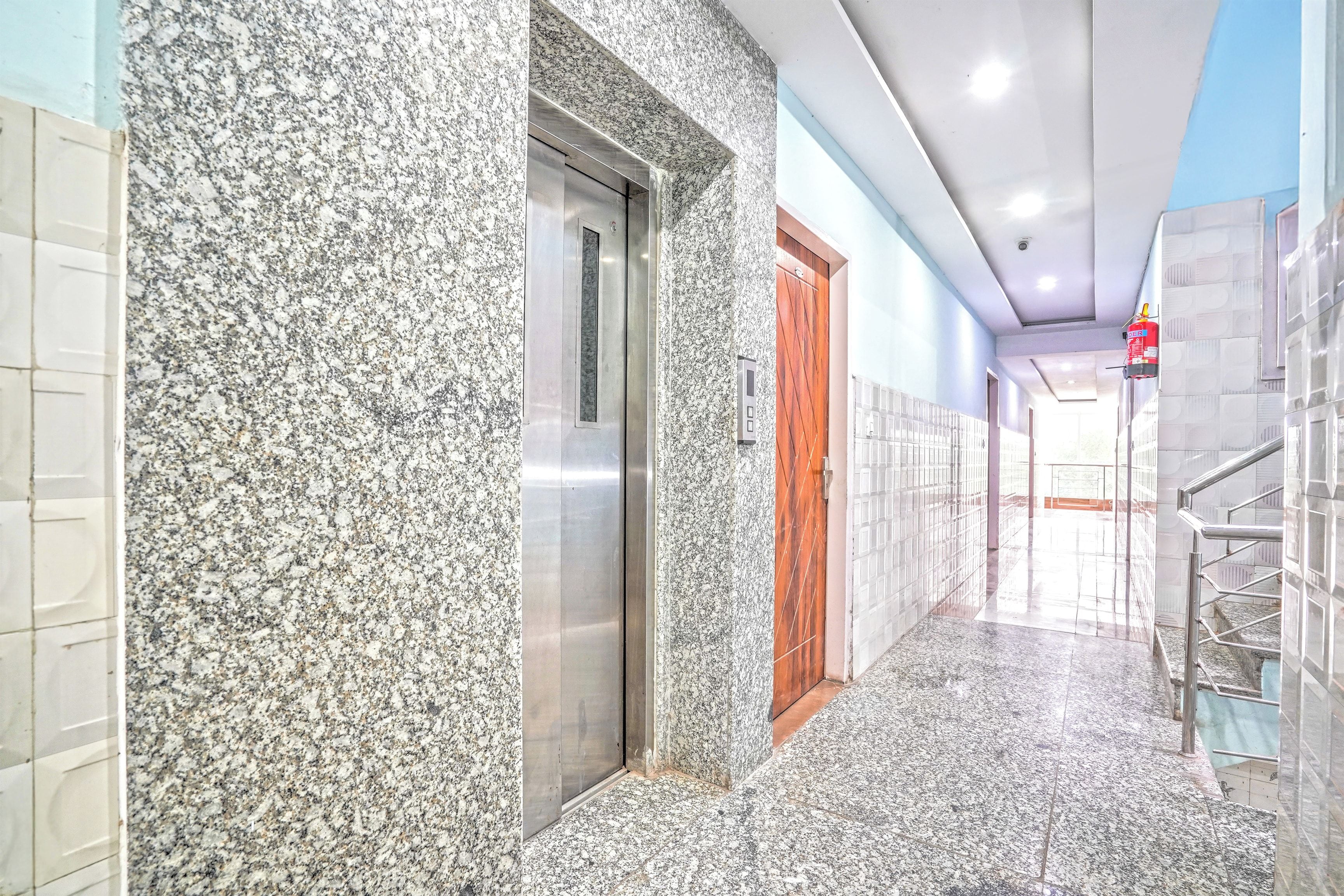 Corredor com parede de granito, porta de madeira e extintor fixado na parede.