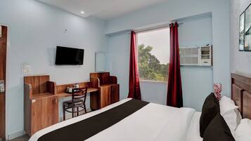 A hotel room with a bed, a desk, a chair, a television, and a window with curtains.