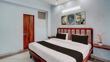 Habitación de hotel con cama de madera, mesita de noche, teléfono en la pared y tres cuadros abstractos.