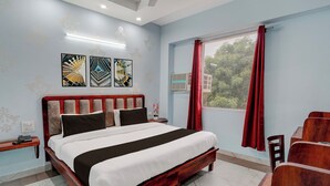 A hotel room with a bed, a nightstand, a telephone, a window with red curtains, and artwork on the wall. - Super Hotel O by OYO Fountain Chowk (Chandigarh)