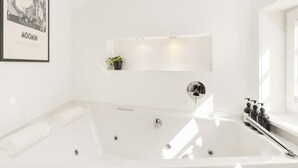 A modern bathroom with a large bathtub, a wall-mounted shelf with a plant, and a framed picture above the tub. - Vrbo Property (Bad Hersfeld)