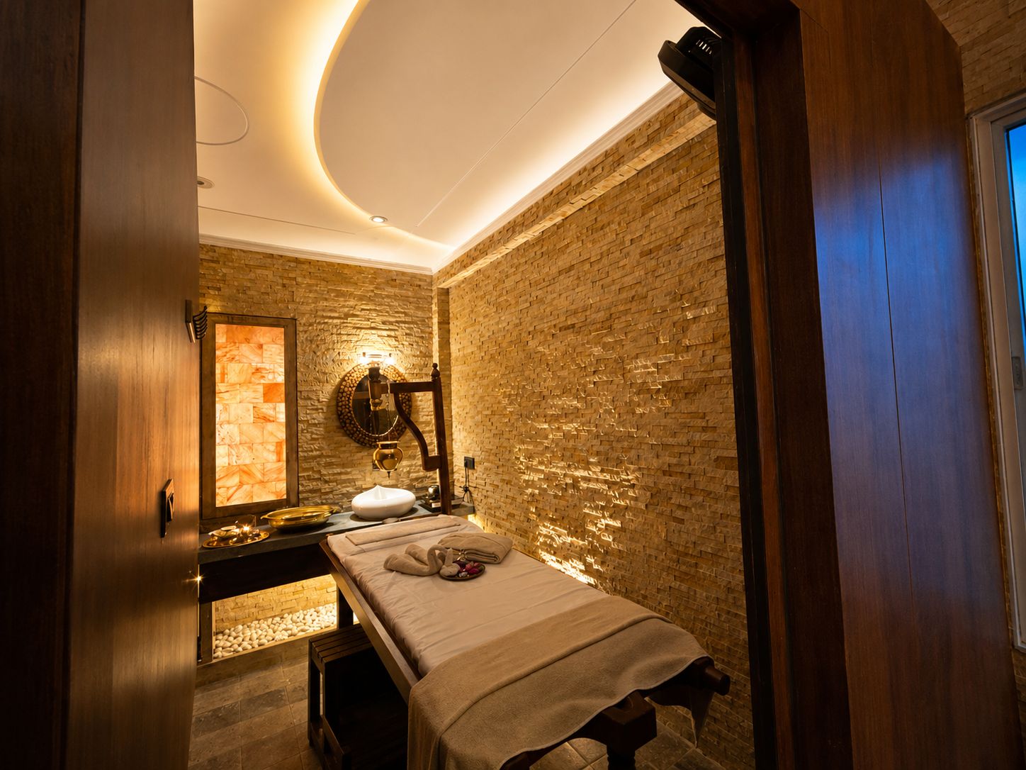 A spa room with a massage table, a stone wall, and a wooden bench.