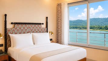 A hotel room with a bed, a nightstand, a lamp, a window with a view of a lake and mountains.