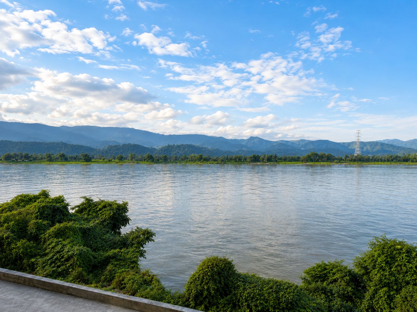 A river with mountains in the background and a power line tower on the right.